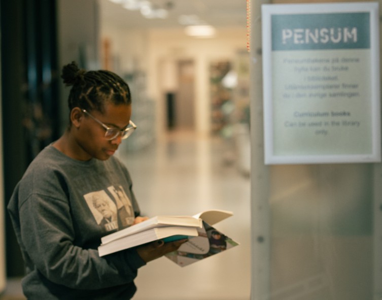 Kvinnelig student leser en bok ved en bokhylle