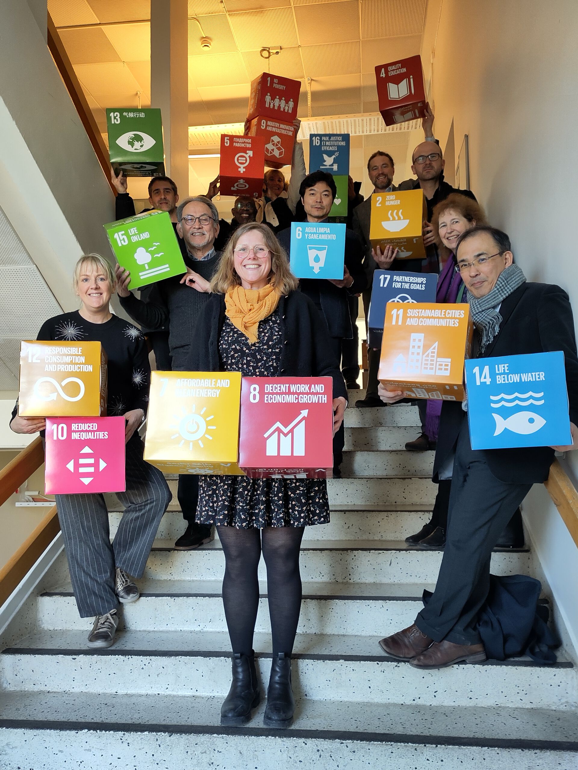 Medlemmer av den internasjonal rådgivende gruppe står i en trapp og holder FNs bærekraftsmål