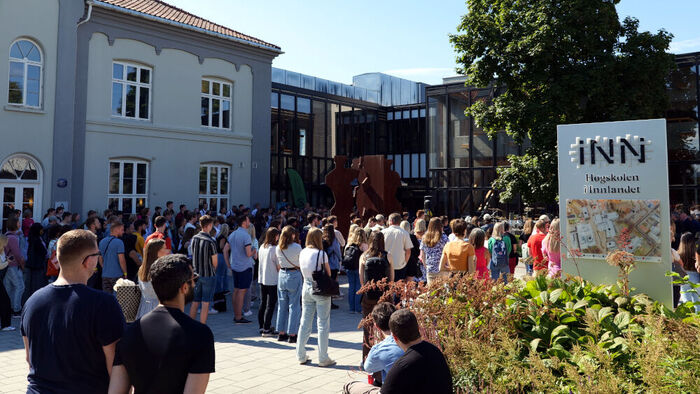 A crowd of students gathered in front of INN University's building in Hamar, a sign with the institutional logo is visible.