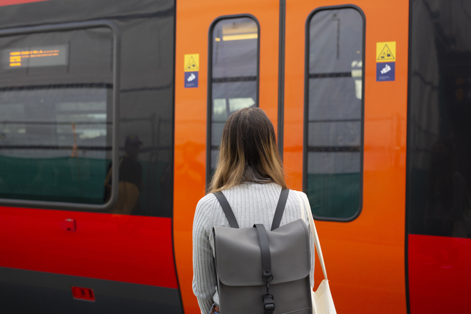 A woman with a backpack stands in front of the doors of a train.