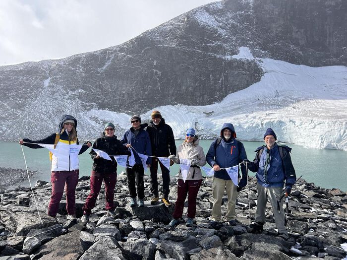 seven people with flags in front of a white glacier with blue water beneath