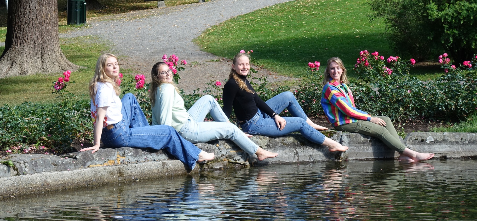 Female exchange students sitting at the pond in the sun with pink roses in the background