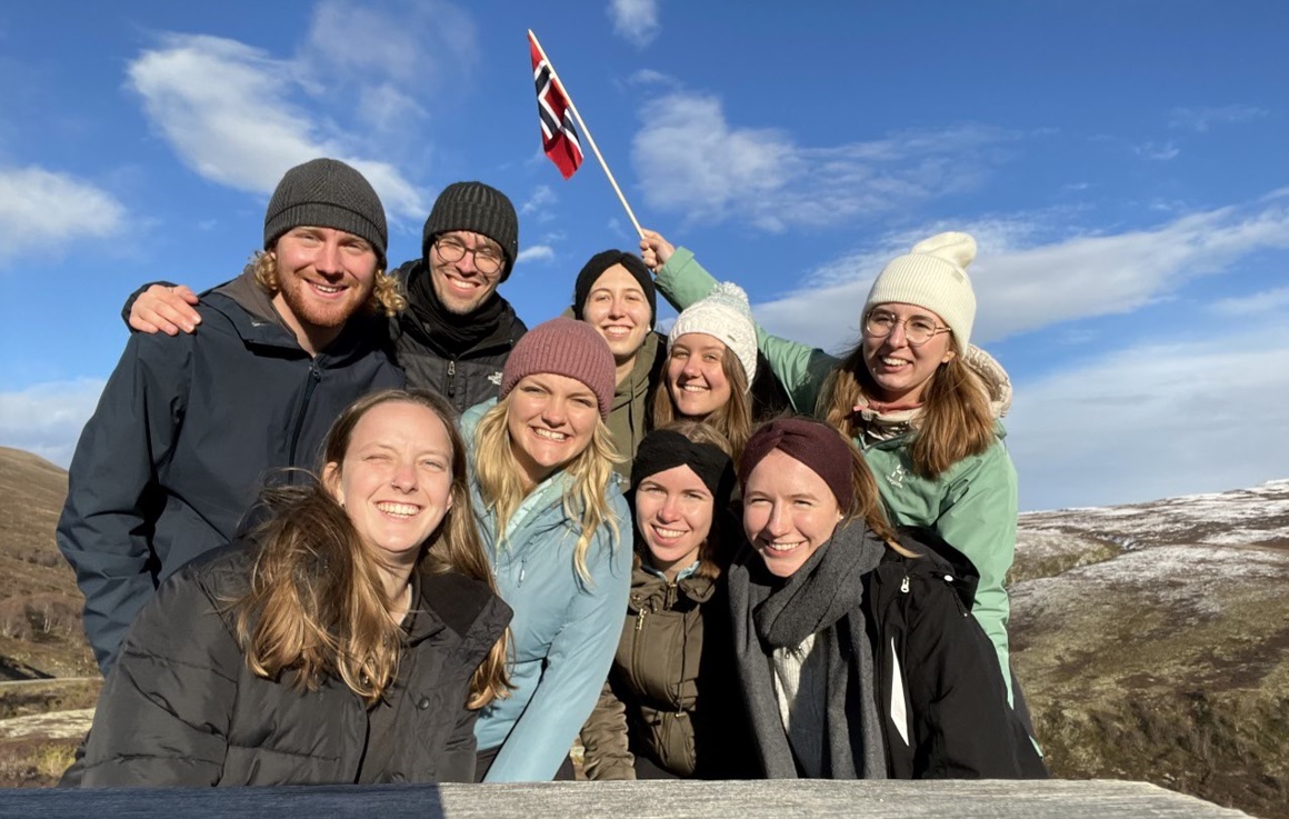 Group of exchange students eaving the Norwegian flag with blue sky in the background