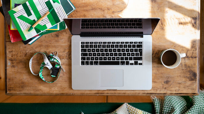 En laptop, kaffekopp, notatbok, penn og nøkkelknippe i bånd ligger på et skrivebord