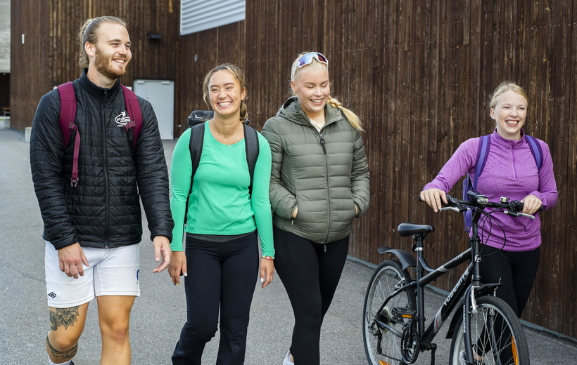 Fire studenter utenfor Terningen arena. En mannlig student i shorts, ei jente med sykkel. Alle fire i munter samtale.