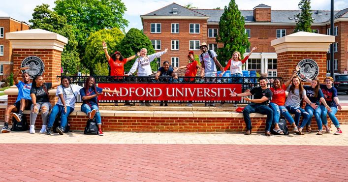 Students sittining next to and standing behind the Radford University sign. They greet you welcome.