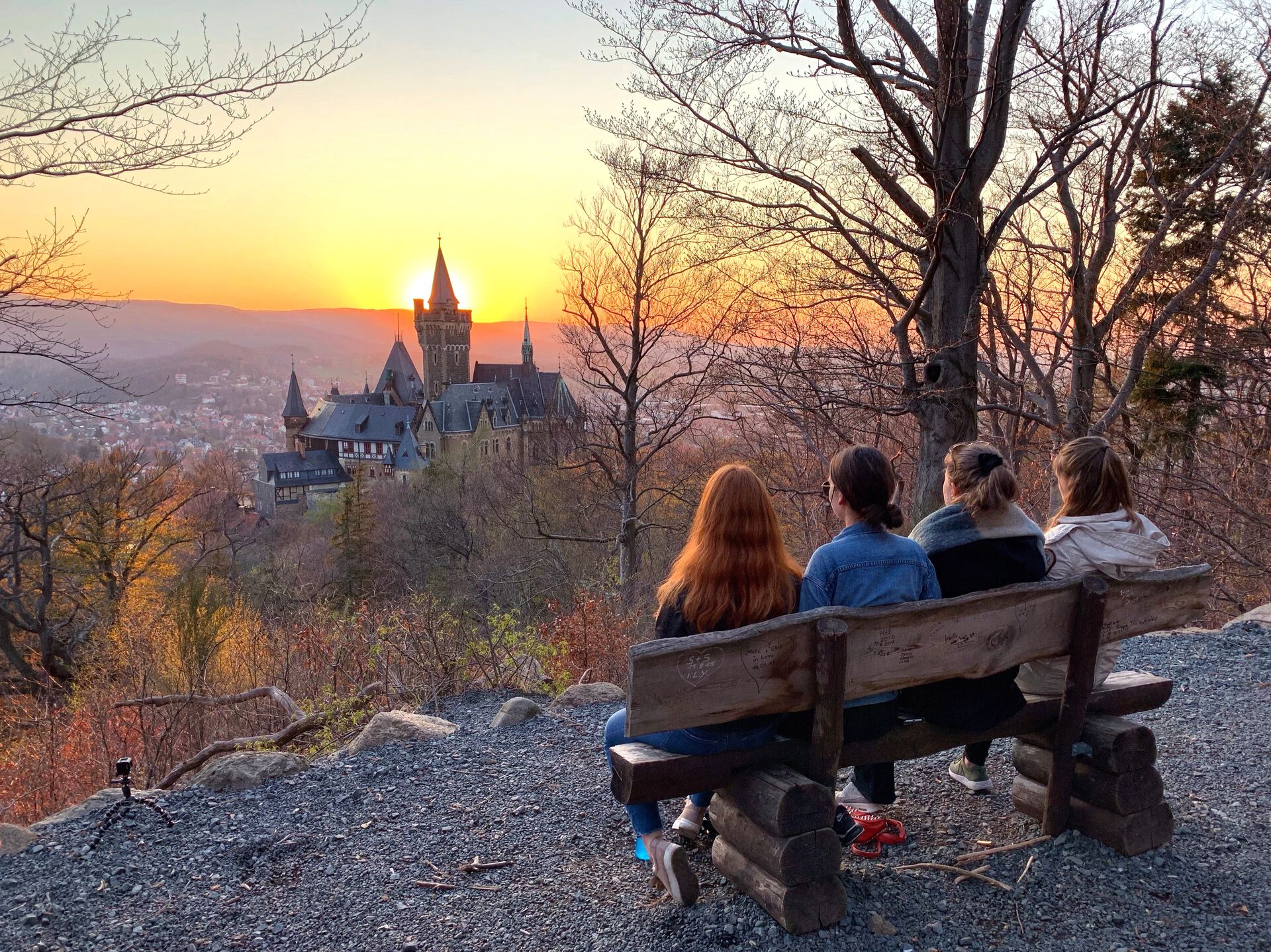 Fire studenter sitter på en benk og ser på utsikten over et slott i solnedgang.