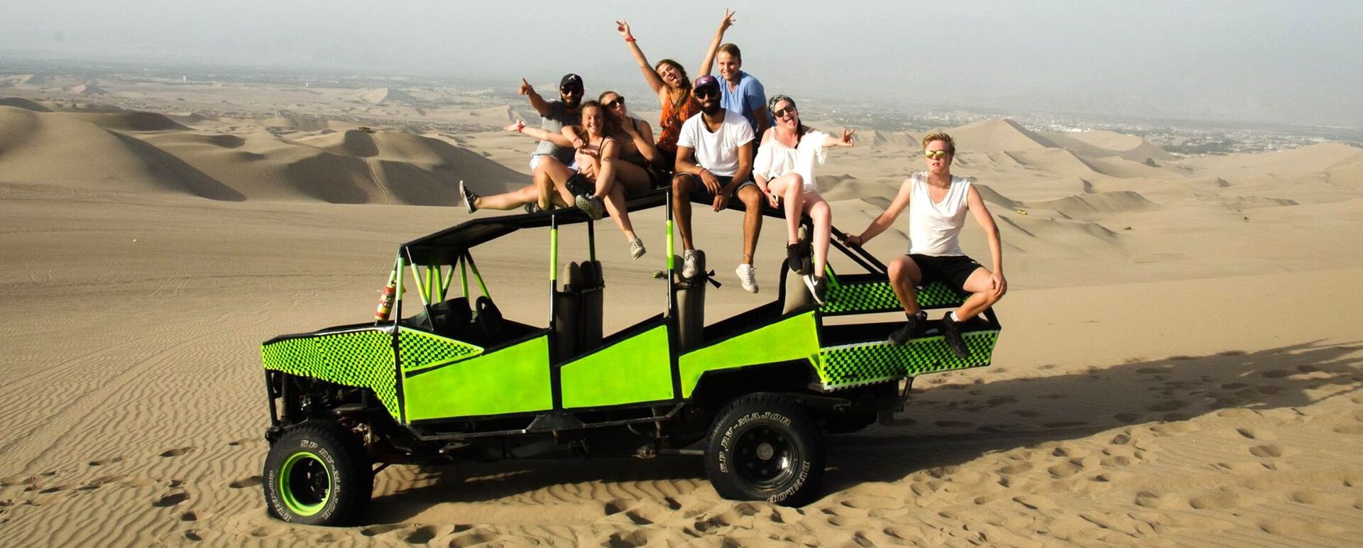 8 studenter sitter på et åpent kjøretøy i et ørkenområde.