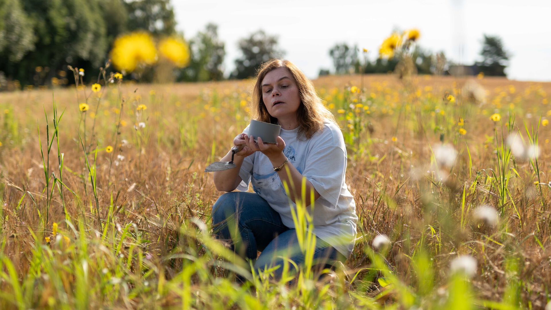 Anna Beata Seniczak sitter i en åker med gule blomster i forgrunnen.