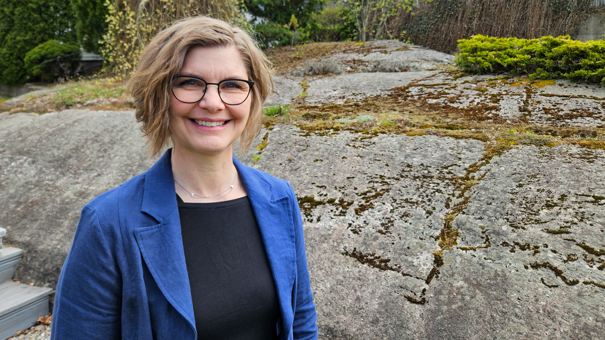 Hilde with a blue jacket and black jumper in front of a rock