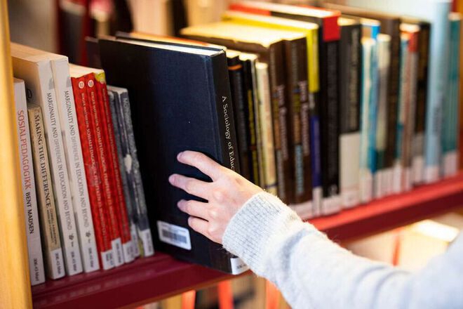 A closeup of a hand reaching for a book in a library bookself.