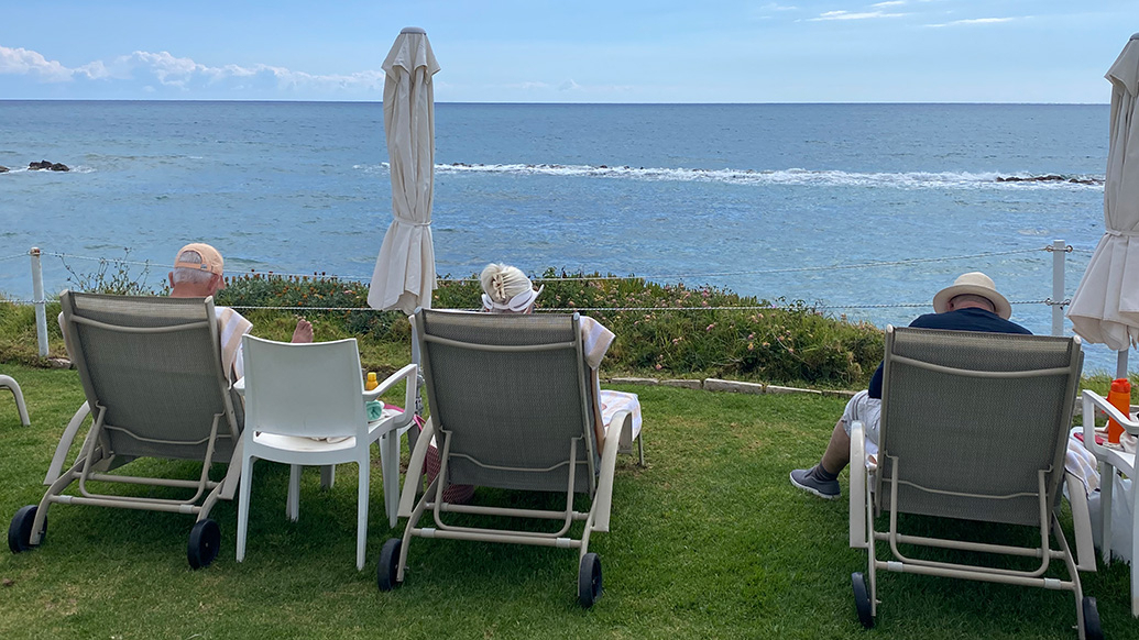 3 solstoler på en plen ved en strand med tre eldre personer.