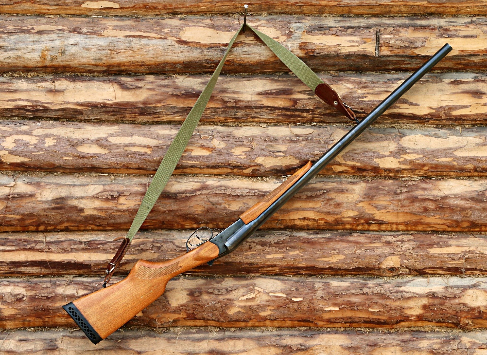 Bilde av et gevær som henger etter reima mot en tømmervegg