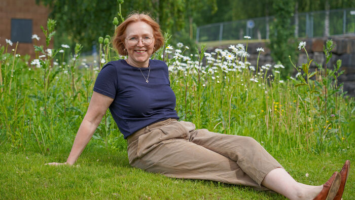 Ingeborg Flagstad is lying down on green grass in front of a flower field. She is happy.