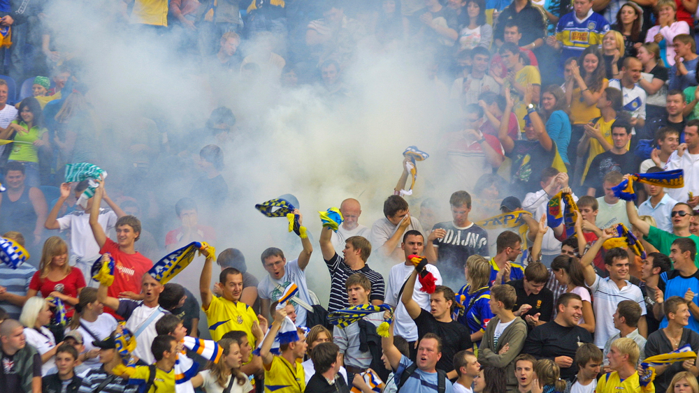 Engasjerte og ropende supportere på en fotballkamp med bluss og flagg