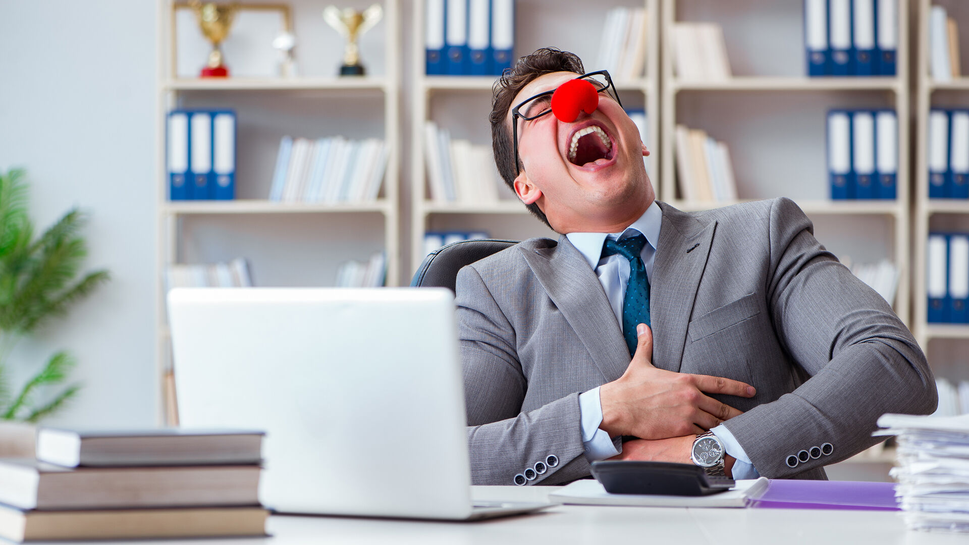 Mann med rød nese sittende bak en PC ler