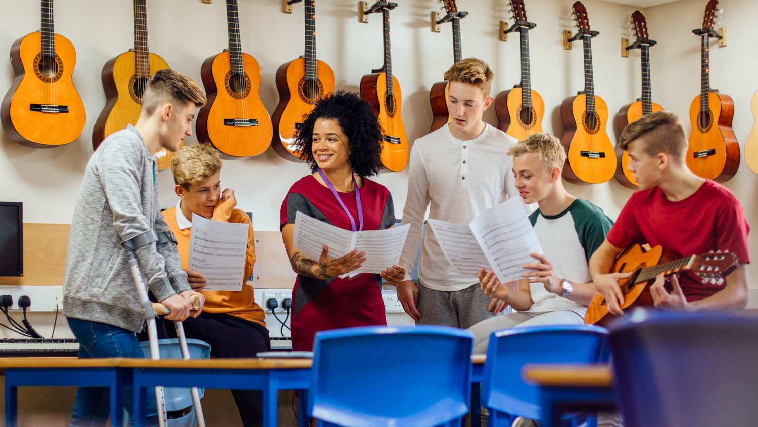 Noen ungdommer har musikkundervisning foran en vegg av gitarer