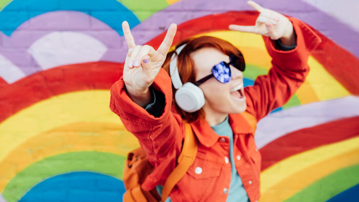 A girl with headphones and sunglasses is dancing in front of a rainbow background