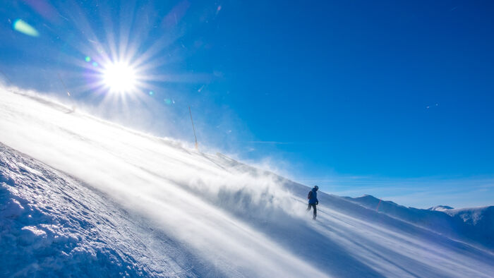 Person på ski i en bratt fjellside med strålende sol. 