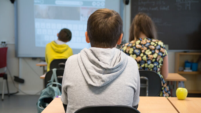 Bilde av en gutt bakgra ved en pult i et klasserom
