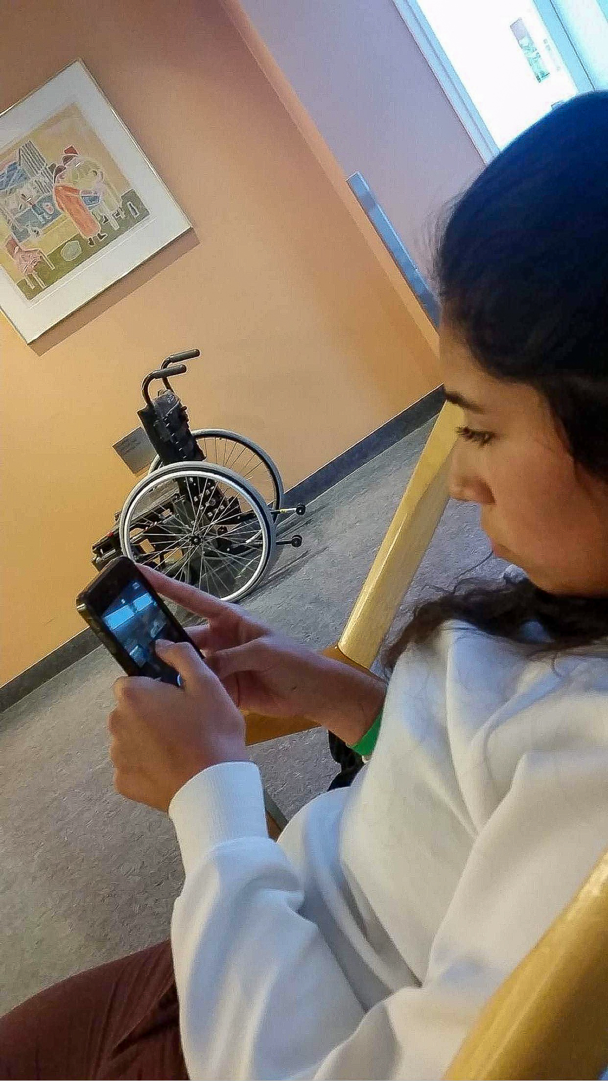 Maria i en sjukehusgang der hun ser på mobilen sin.
