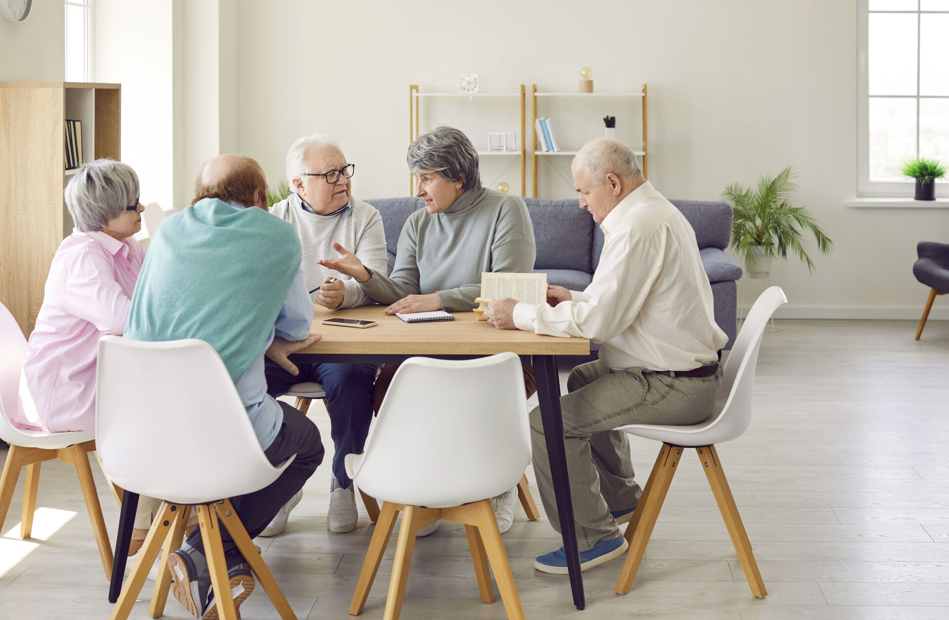 En gruppe eldre mennesker som sitter rundt et bord og snakker sammen.
