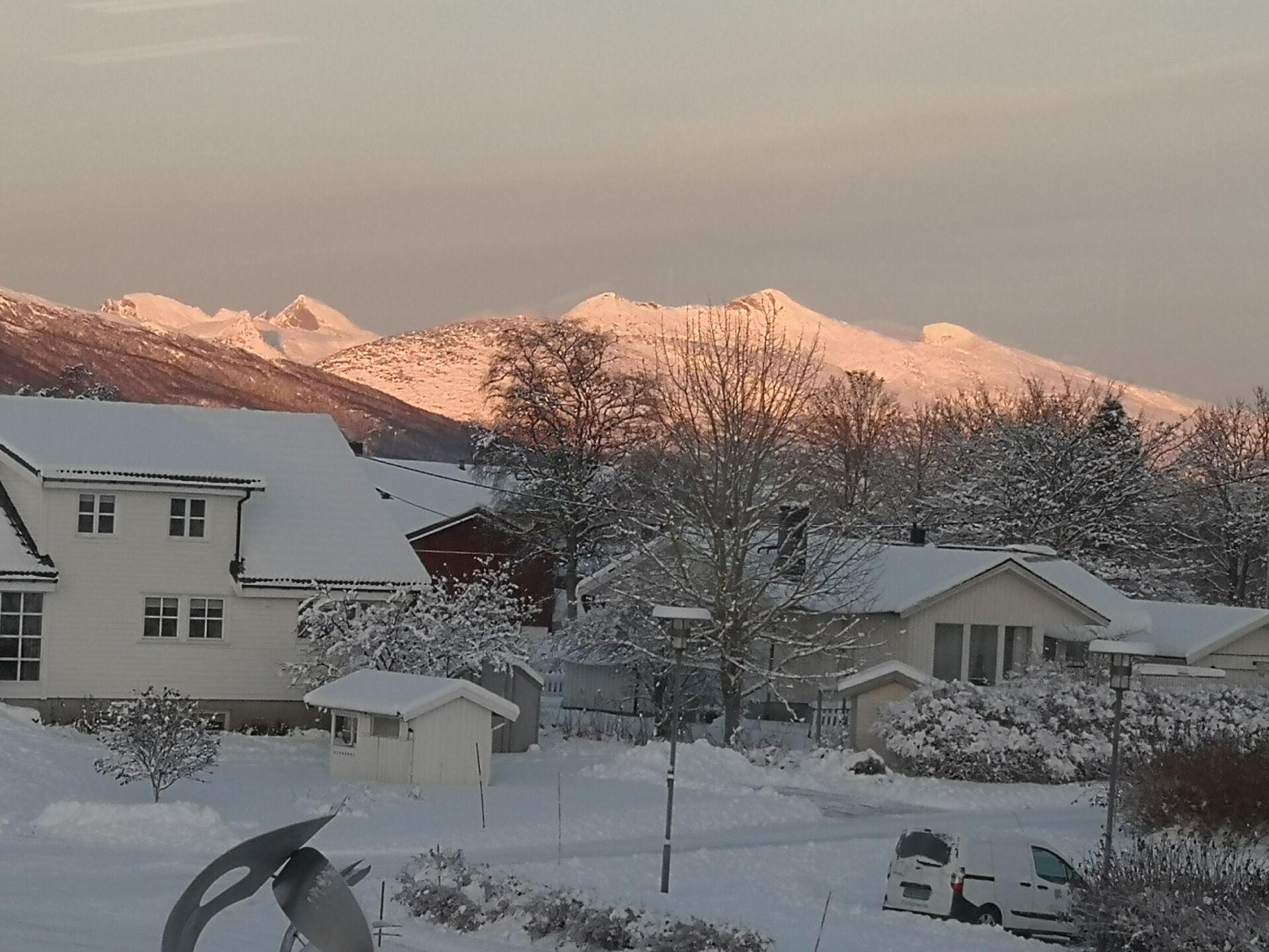 hvit hus foran hvite fjelltopper og snø, sol på fjellet med flott vinterlys