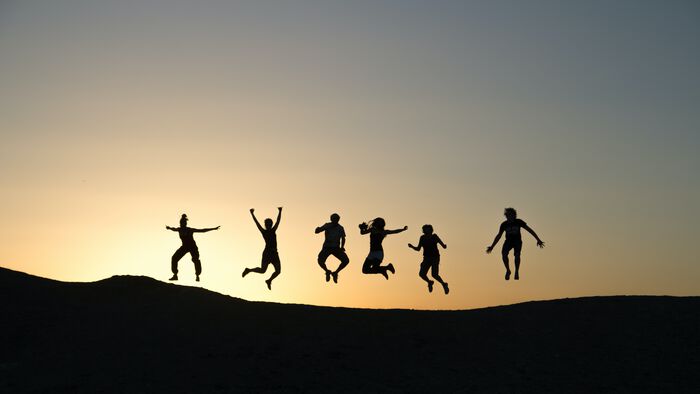 seks personer som hopper i lufta foran en gul farget himmel