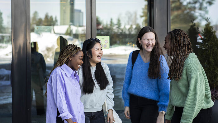 Fire kvinnelige studenter utenfor Terningen Arena. De smiler og le er mens de prater med hverandre. 