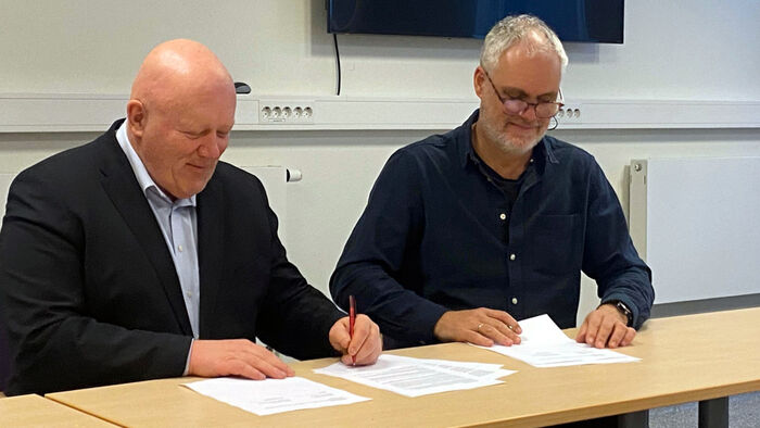 Peer Jacob Svenkerud og Yngvar Åsholt sitter ved et bord og signerer avtaledokumentene