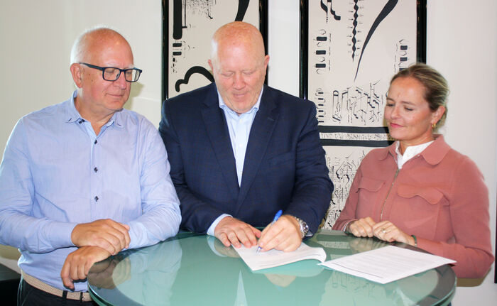 Per Arne Tufte, Peer Jacob Svenkerud og Anette Mellbye står ved et bord med Svenkerud signerer avtaledokumentet