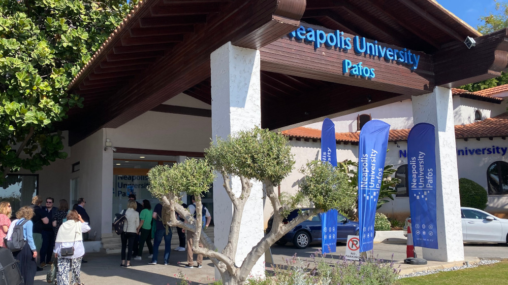 Flere personer foran inngansgpartiet til Neapolis University Phaphos, med navn og logo på veggen