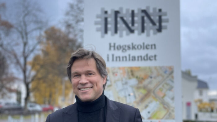 Leif Holst Jensen i svart dressjakke står utendørs foran et skilt med høgskolens logo
