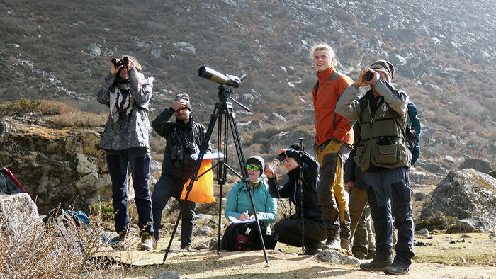 Seks studenter ute i felt i Nepal. De har kikkerter og ser ut i horisonten. 