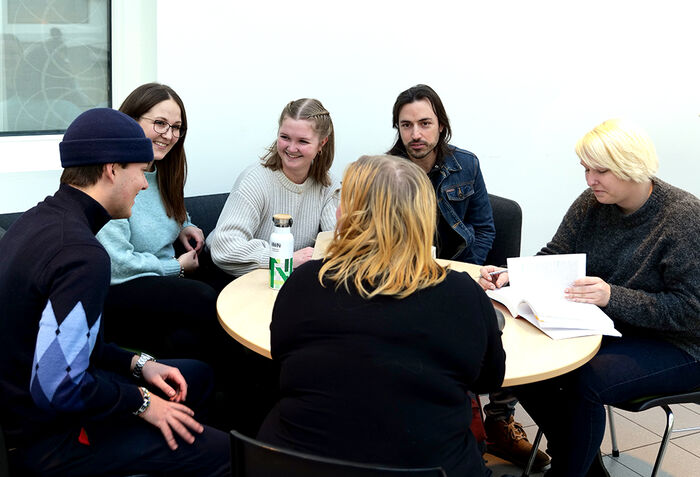 Bilde av seks studenter som sitter rundt et bord og diskuterer.
