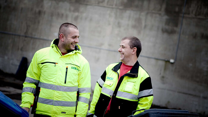 To renovatører i gule jakker som smiler til hverandre. 