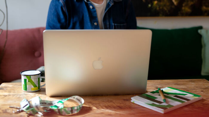 En person sitter i bakgrunnen ved et bord med en laptop, notatblokk og en kopp foran seg