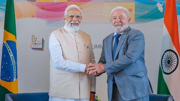Indias statsminister og Brasils president tar hverandre i hånden og ser tilfreds i kamera. De er flankerte av landenes to flagg.