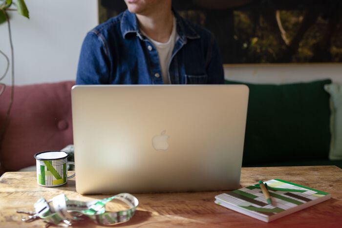 person foran mac laptop med kopp og nøkkelring i HINNs profilfarger grønn og hvit rundt seg på bordet
