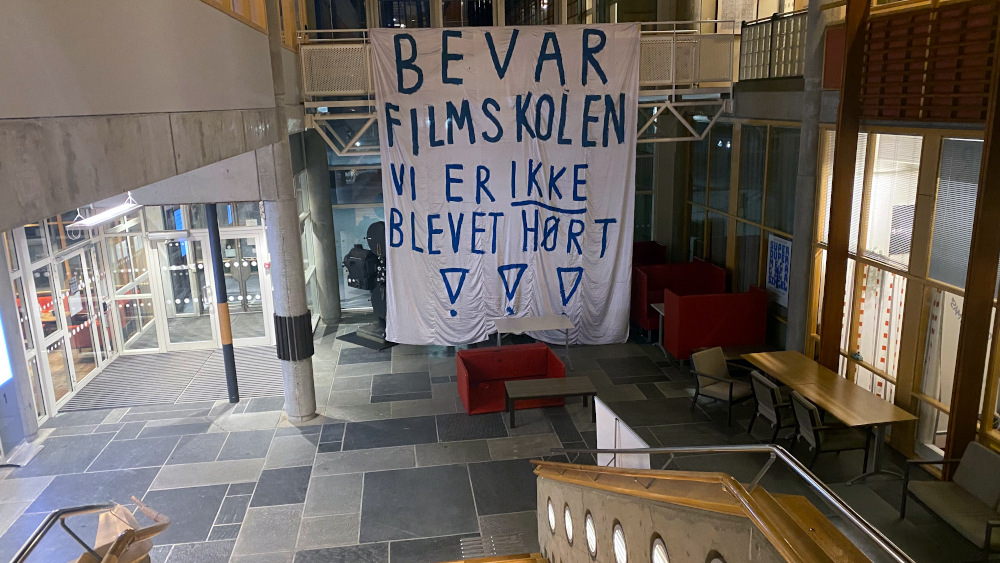 Et banner med teksten "bevar filmskolen - vi har ikke blitt hørt" henger fra taket i høgskolens lokaler