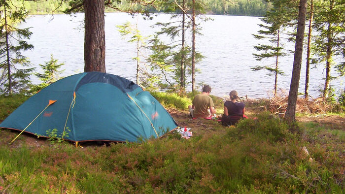 telt ved innsjø i skogen med to personer som sitter ved siden av