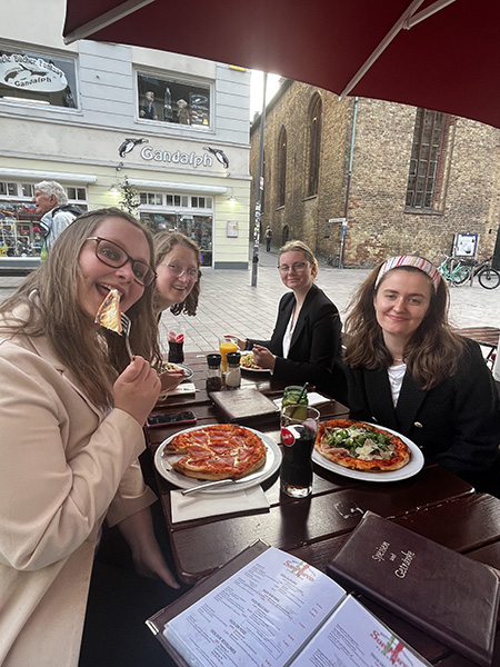 Fire studenter spiser pizza på en restaurant i en idyllisk gågate