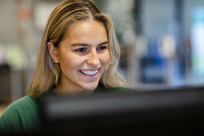 Nærbilde av en blid, kvinnelig student som ser fornøyd på en PC-skjerm