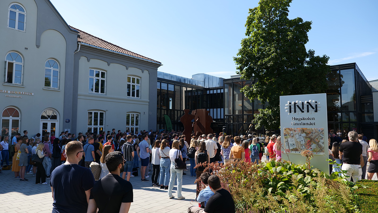 En stor forsamling med studenter står samlet utenfor studiested Hamar på en sommerdag, og følger med på åpningssermonien
