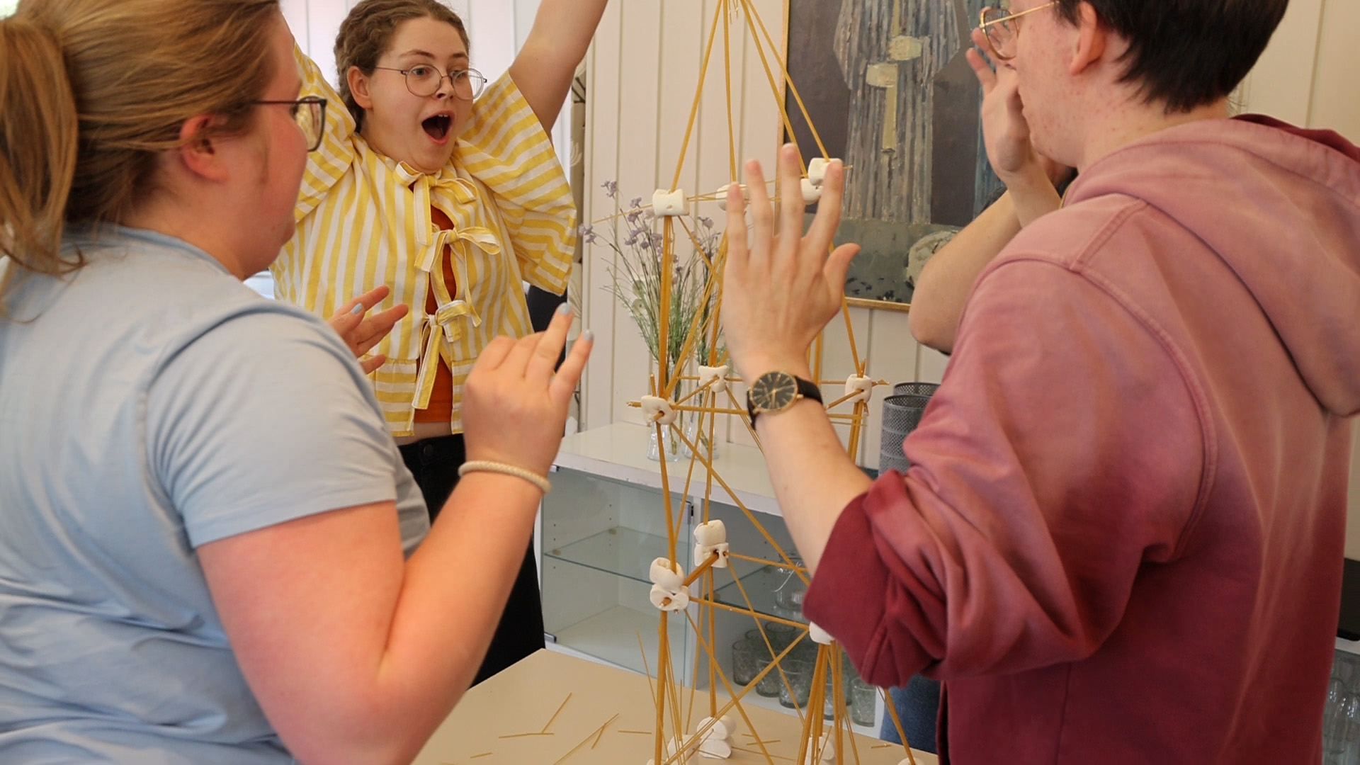 Tre studenter er begeistret over at tårnet laget av spagetti og marshmallow fremdeles står etter at de har sluppet taket på dem