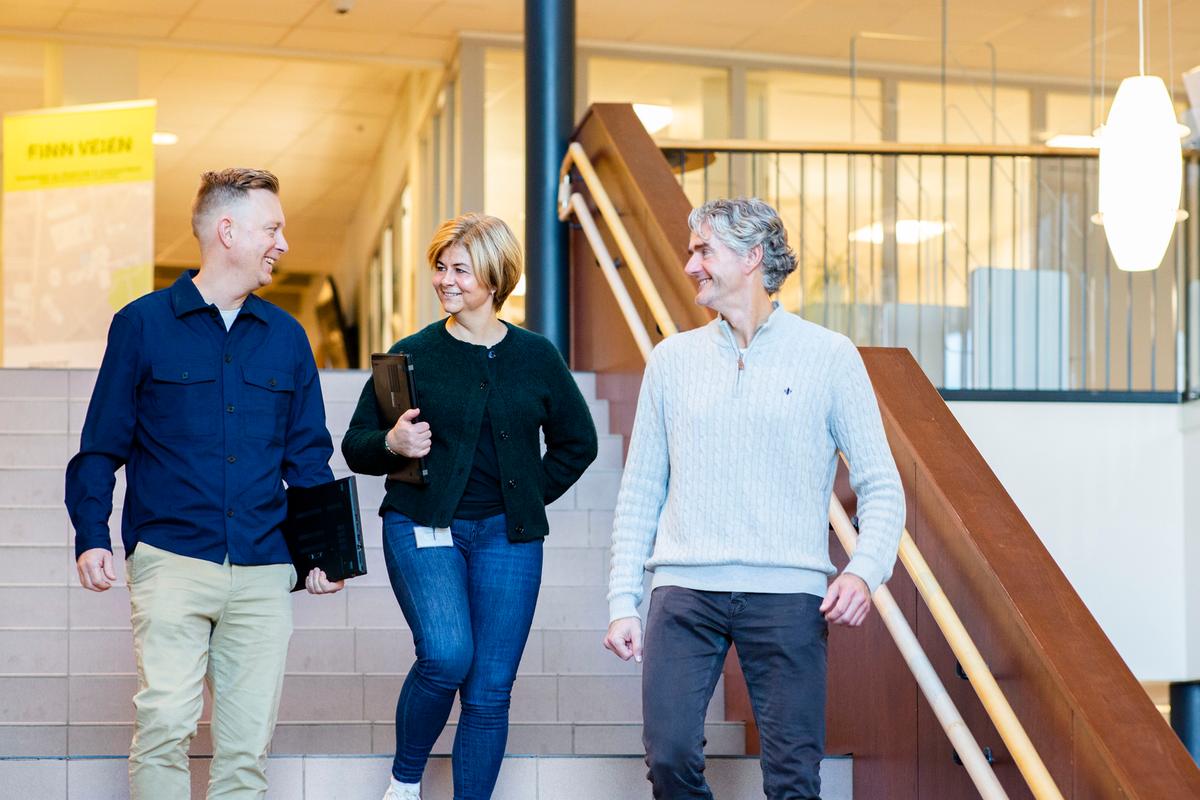 Pål, Rita og Espen går ned en trapp på campus Hamar. De smiler og ler mot hverandre.