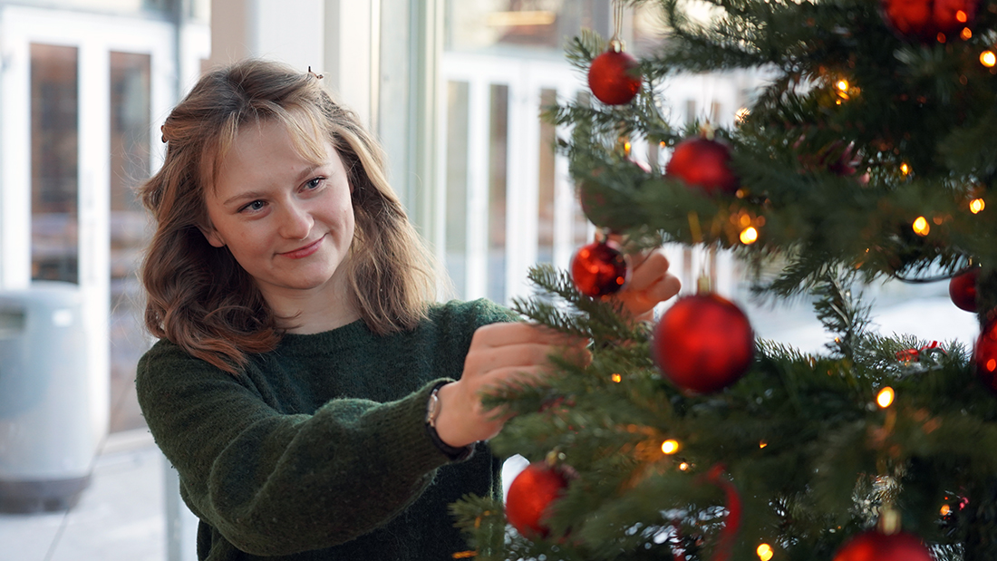 Portrettfoto av en kvinnelig student som pynter et juletre. 