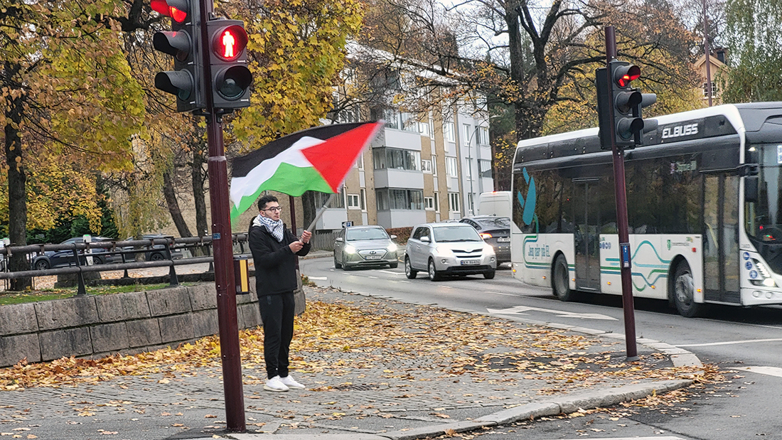 Mann som står med et palestinsk flagg i et lyskryss. 