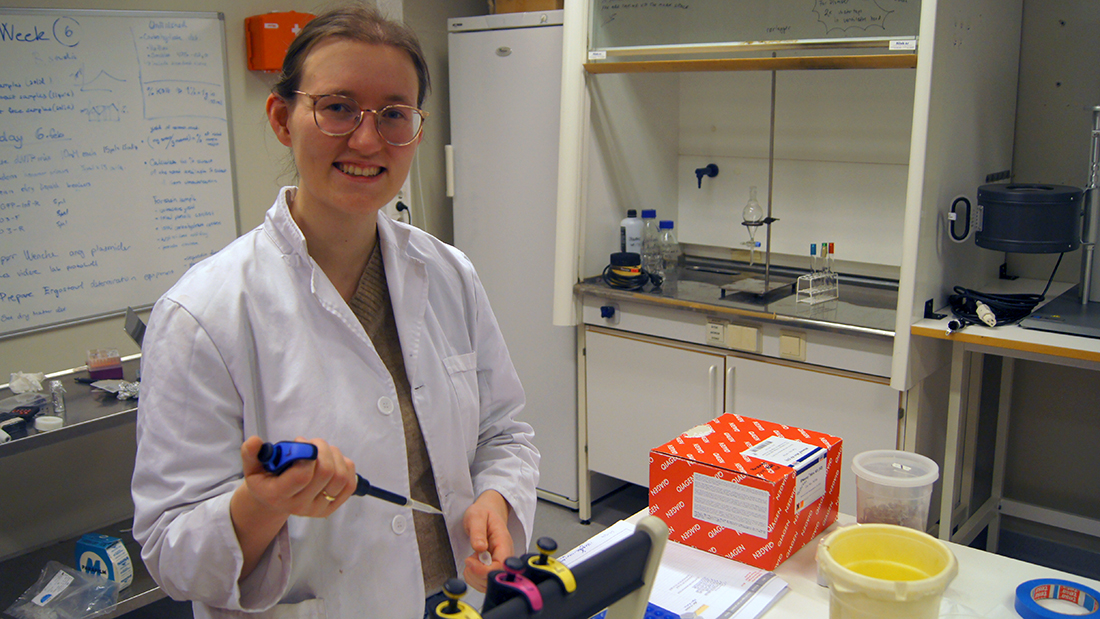 A female student wearing a white lab coat in a lab.