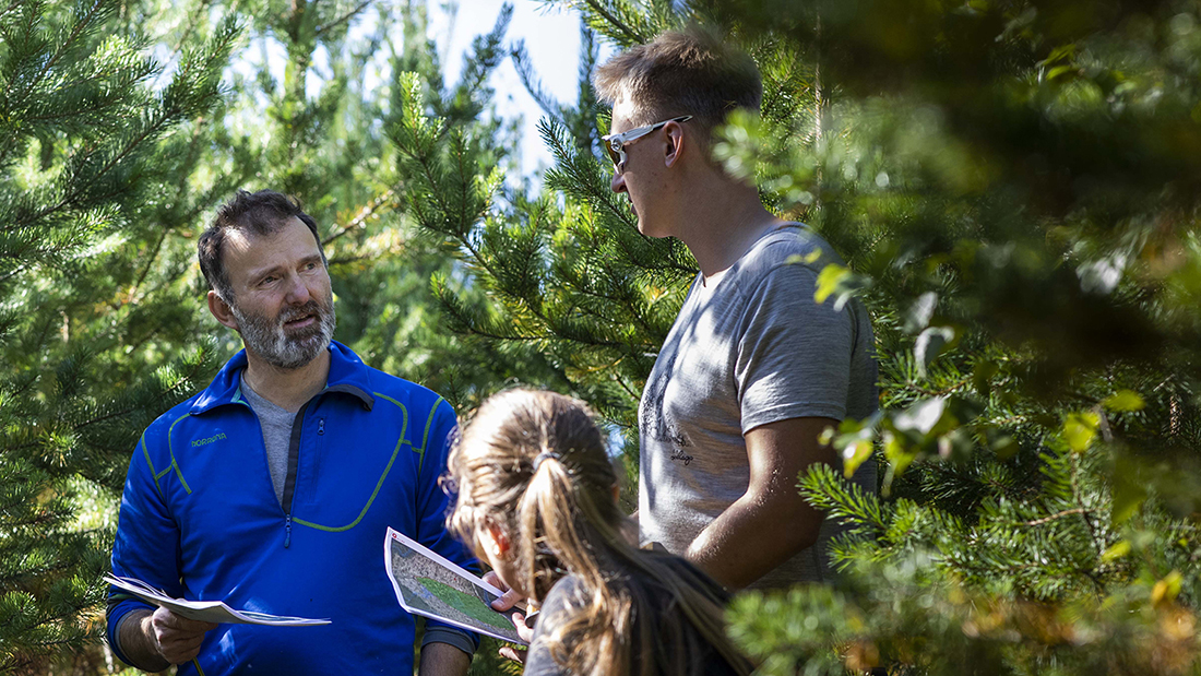 To studenter og en fra fagmiljøet på Evenstad som diskuterer fag ute i skogen. 
